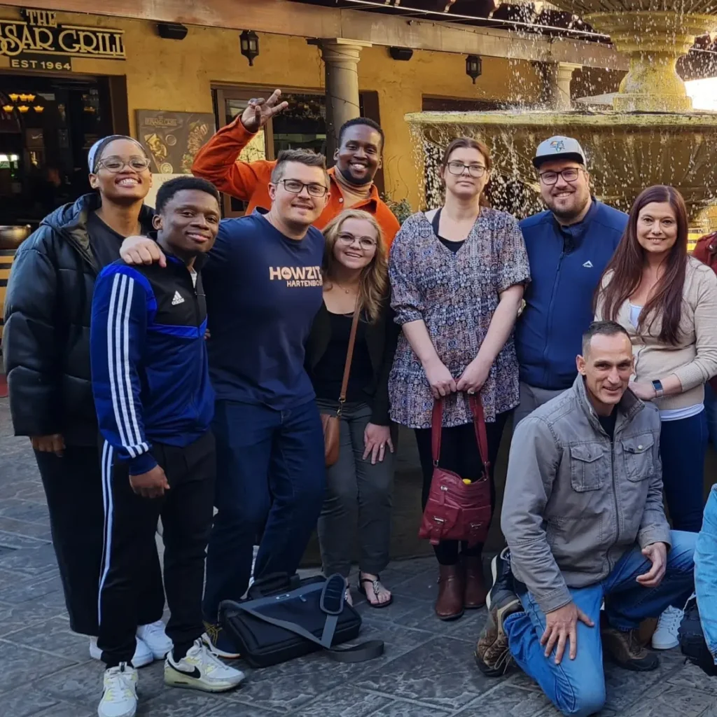 The Nintex Team pose and smile together outdoors in front of a stone fountain. Some people are standing while others kneel, and everyone appears happy on a sunny day.