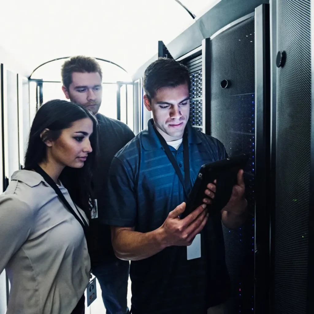 Three people in a secure server room reviewing data on a tablet device.