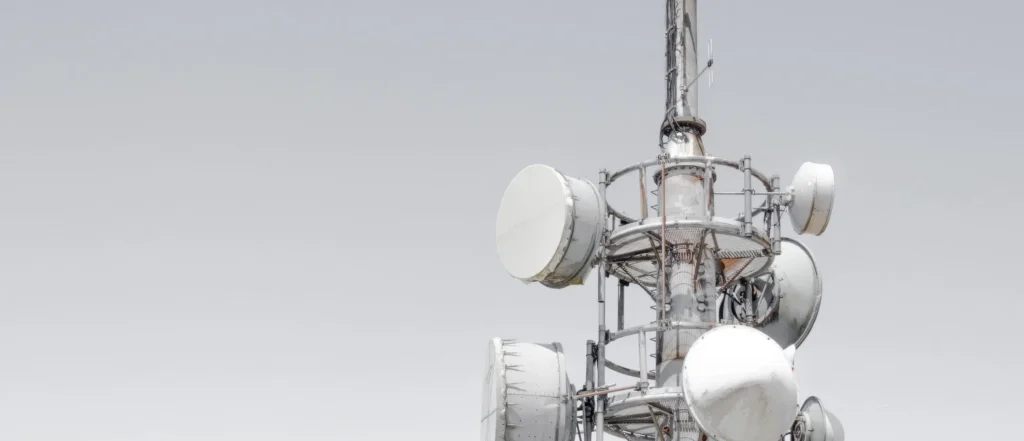 A telecommunications tower stands against a pale, overcast sky. Several round antennas and dishes are visible.