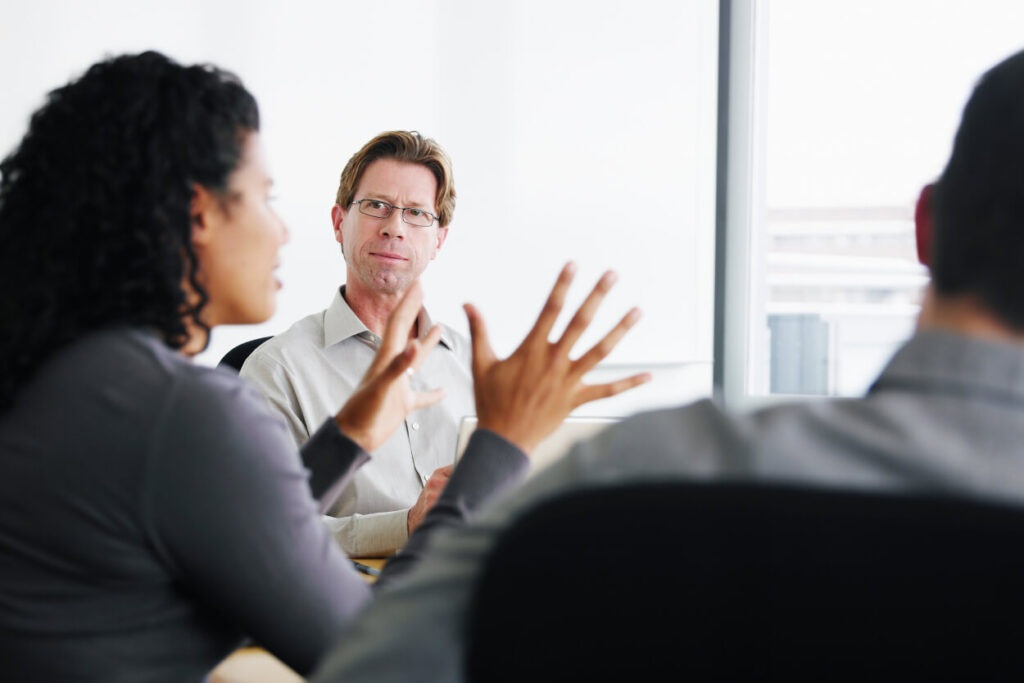 Three people in a glass conference room having a conversation.