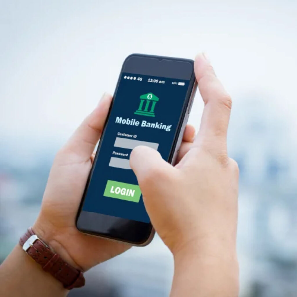 A person holding a smartphone and using a mobile banking app, with fields for customer ID and password visible on the screen and a finger about to tap the login button.