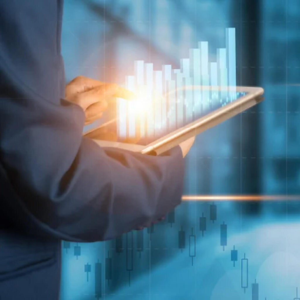 A person in a suit uses a tablet with a glowing screen displaying blue bar graphs and financial charts, representing data analysis or business growth in a digital environment.
