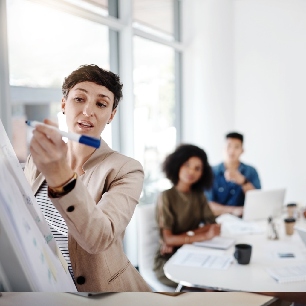 Image of a woman at a whiteboard presenting to others in the office.