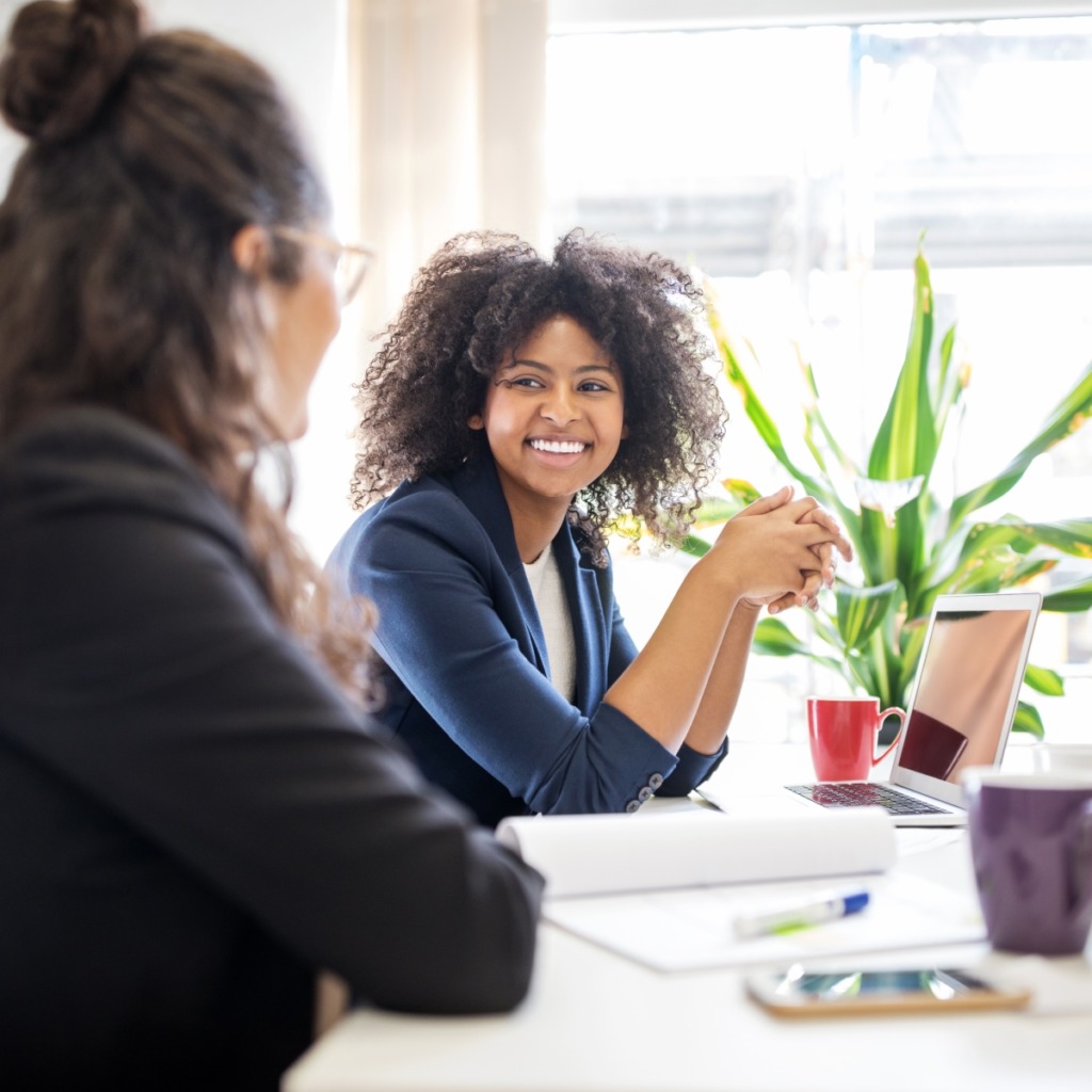 Two woman having a conversation at their desk.
