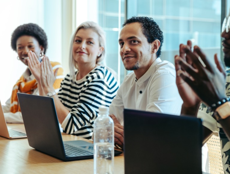 Four coworkers, sitting at a conference table, applauding.